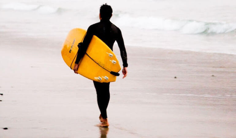 A guy walking with his surf board 