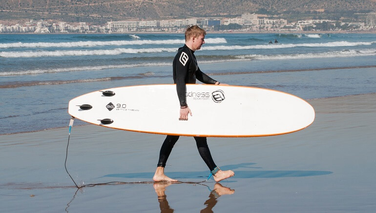 Guy carrying a softboard and walking out of the water after a surf session