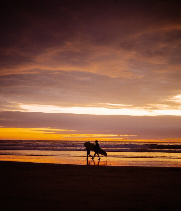 Surfers walking on the beach during the sunset in Montañita, Ecuador