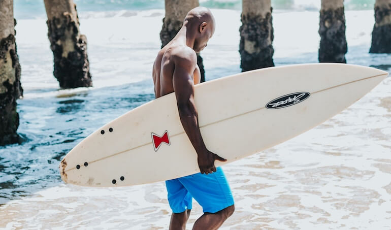 A fit guy walking with his shortboard 