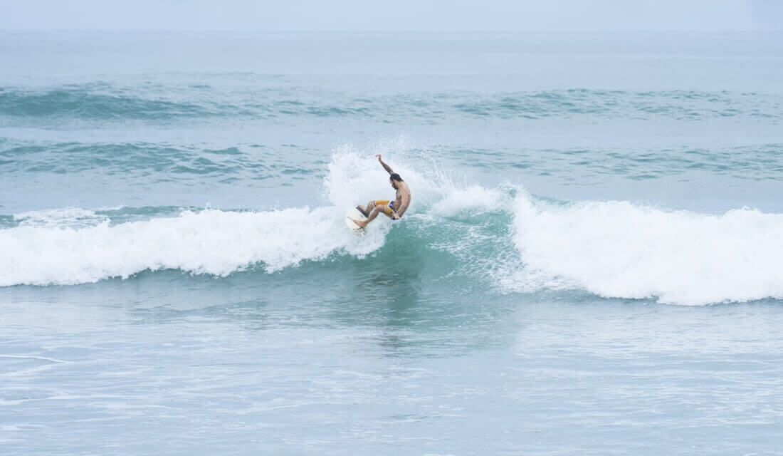 Man riding a surfboard facing the waves on the ocean and beach