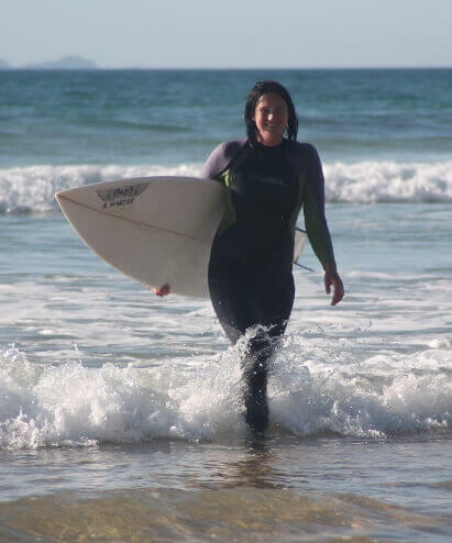 Surfer Moa Ailert in a wetsuit coming out of the water after a surf session. She is smiling